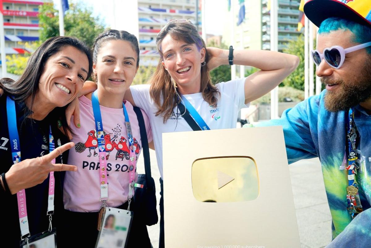 One male and three female athletes are posing with the golden plaque that is awarded to YouTube accounts with more than 1 million subscribers